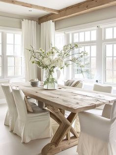 a dining room table with white chairs and flowers in a vase on the top of it