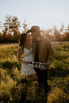 a man and woman are standing in the grass holding a box with pictures on it