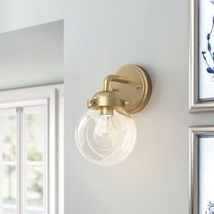 a bathroom light that is on the wall next to a window with flowers in it