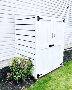 a white storage shed sitting next to a flower bed on the side of a building