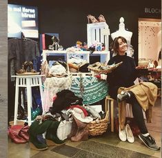 a woman sitting in front of a pile of shoes and bags next to a table