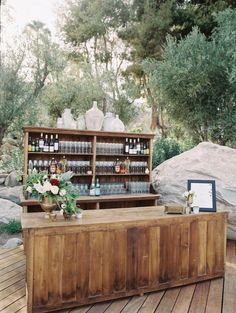 an outdoor bar is set up with bottles and vases on the counter, along with flowers