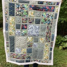 a person holding up a quilt made from old patchwork fabrics in front of some trees