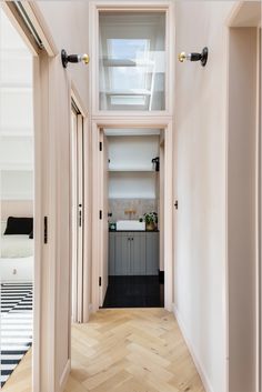 an empty hallway leading to a bedroom with white walls and wooden floors, along with black and white striped rugs