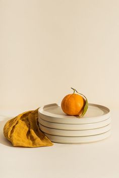 an orange sitting on top of three white plates next to a yellow napkin and a piece of cloth