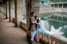 a man and woman standing next to each other on a bridge over water with stone steps