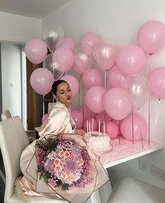 a woman sitting at a table with pink balloons and cake in front of her,