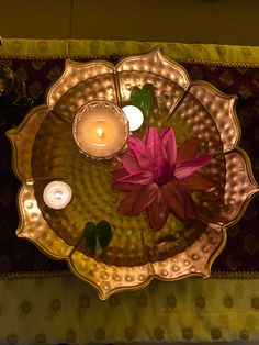 a candle and some pink flowers on a gold plate with candles in the middle,