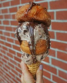 a person holding up an ice cream cone with chocolate and vanilla toppings in front of a brick wall