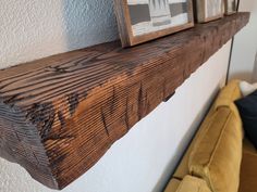 a close up of a wooden shelf with two pictures on the wall above it and a couch in the background