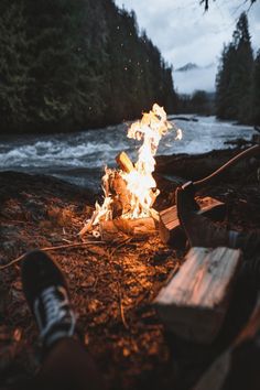 a person sitting in front of a campfire with their feet on the ground next to it