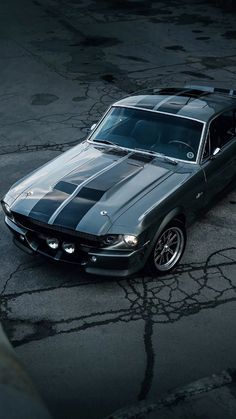 an old mustang muscle car parked in a parking lot with the hood up and stripes painted on it