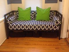 a couch with two green pillows on top of it in front of a window and wooden floor