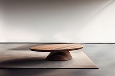 a round wooden table sitting on top of a floor next to a white wall in an empty room