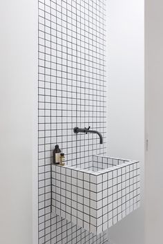 a white bathroom with black and white tiles on the wall, sink and shower faucet