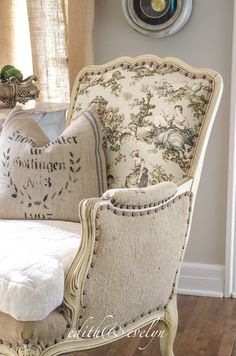 an old chair with pillows on it in front of a wall clock and window sill