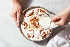 a person pouring milk into a pan filled with cinnamon rolls