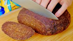 a person holding a knife over a loaf of bread on top of a wooden cutting board