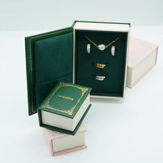 an open box with jewelry inside on a white surface next to two other boxes that have rings and necklaces in them