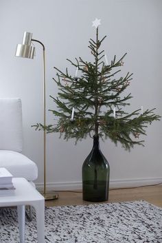 a living room with a christmas tree in a green vase on the floor next to a white couch