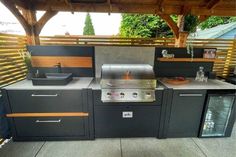 an outdoor kitchen with grill, sink and cabinets on the outside patio in front of a pergolated roof