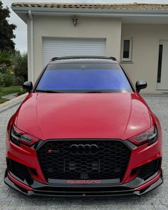 the front end of a red car parked in front of a house with a garage door