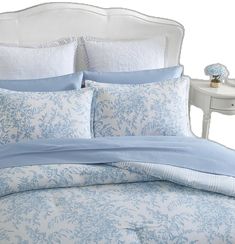 a bed with blue and white comforters on top of it next to a night stand