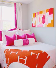 a bed with pink and white pillows in a bedroom next to a window that has an orange blanket on it