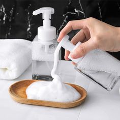 someone is pouring soap into a wooden bowl on a white counter with towels and other items