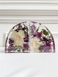 two glass vases with flowers in them sitting on a white tableclothed surface