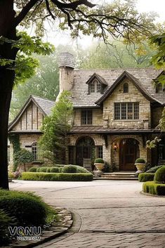 a large stone house surrounded by trees and bushes in front of a tree filled driveway