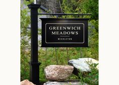 a sign for greenwich meadows in front of some rocks and bushes with trees behind it