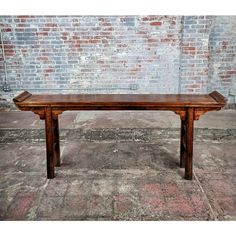 a wooden bench sitting on top of a cement floor next to a brick wall in an old building