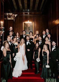 a large group of people in formal wear posing for a photo on the red carpeted stairs