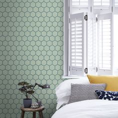 a bedroom with green wallpaper and white shutters on the window sill, next to a small table with a potted plant