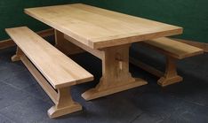 a wooden table with two benches next to it on a tile floor in front of a green wall