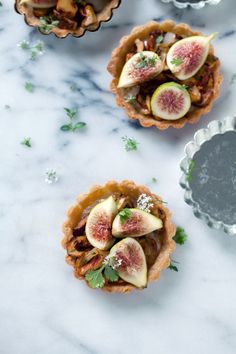 three small pies filled with fruit on top of a marble counter next to silver dishes