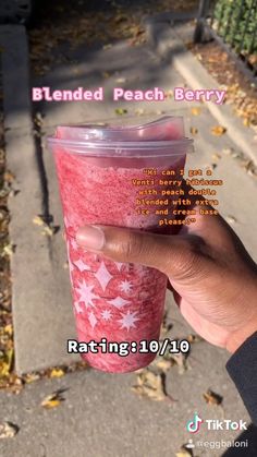 a person holding up a plastic cup with pink liquid in it and the words blended peach berry