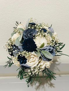 a bridal bouquet with blue and white flowers on a shelf next to a wall