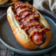 a hot dog with bacon on it sitting on a plate next to some buns