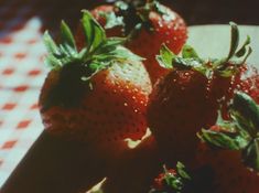 three strawberries sitting on top of a white and red checkered table cloth with green leaves