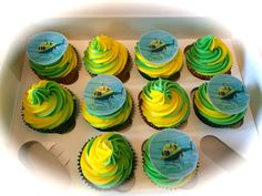 twelve cupcakes with green and yellow frosting in a box on a table