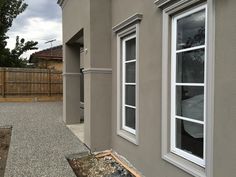 the side of a house with two windows and graveled ground in front of it