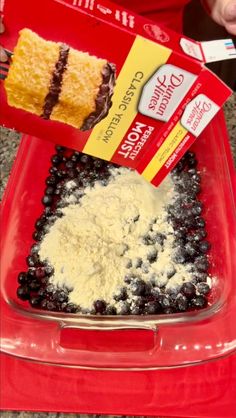 someone is pouring batter into a red container with blueberries and cake mix in it