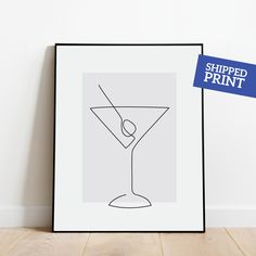 a line drawing of a martini glass on a white wall next to a black framed art print