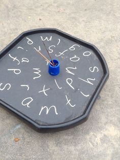 a black clock with white writing on it and two blue cups sitting in front of it