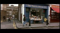 people are walking down the street in front of a travel book shop on a corner