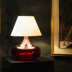 a red lamp sitting on top of a table next to a painting