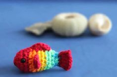 a small crocheted fish sitting next to an egg shell on a blue surface