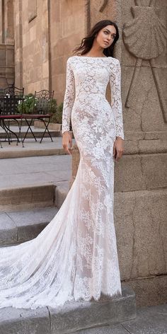 a woman in a white wedding dress standing next to a stone wall with her hands on her hips